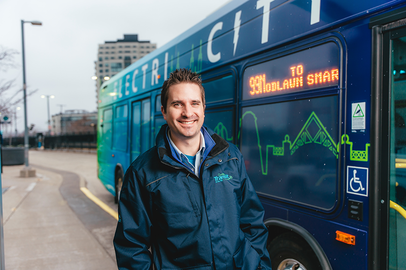 Transit driver standing beside an electric bus
