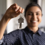 Happy Indian woman ready to move into new home. Real estate agent offering rent or buying house, flat, apartment, help with loan and mortgage. Hand of buyer or home owner holding key. Closeup
